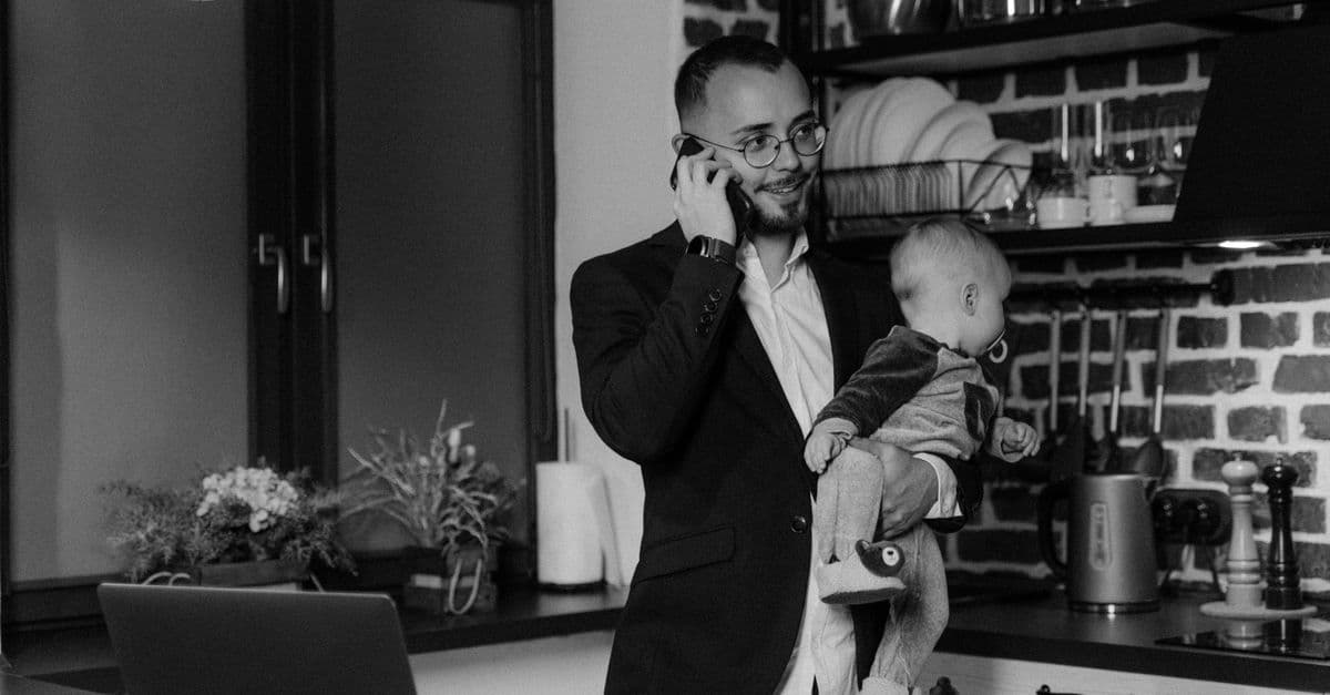 Vater hält sein Baby im Arm und telefoniert gleichzeitig in der Küche