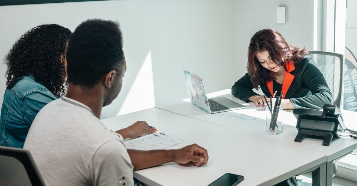 A couple discussing paperwork with an advisor in a modern office setting, showcasing collaboration.