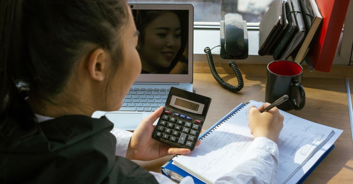 Woman using a calculator at a desk with a laptop and notepad, involved in office work.