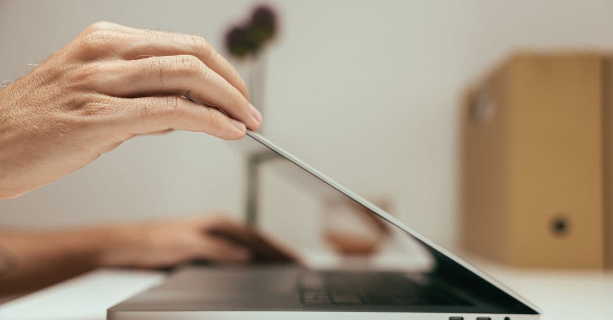 A close-up of a hand closing a laptop in a clean and minimal office setting, symbolizing the end of a work session.