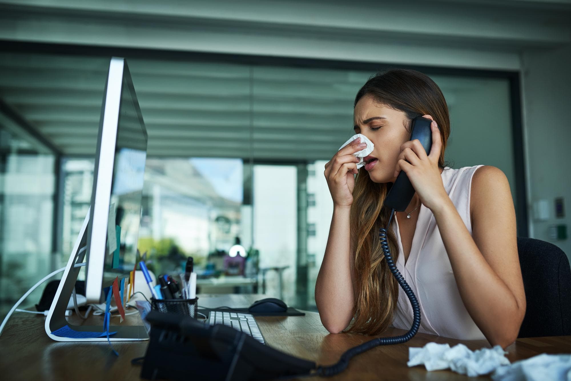 Allergy phone call and business woman with tissue for cold hay fever and infection in office Health corporate administration and person on computer blowing nose for illness flu and sinusitis
