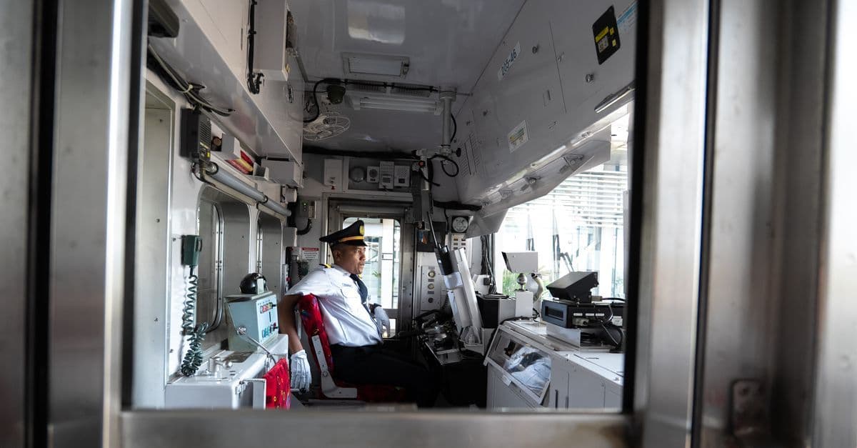 Train operator seated in control room, focused on steering, inside perspective.