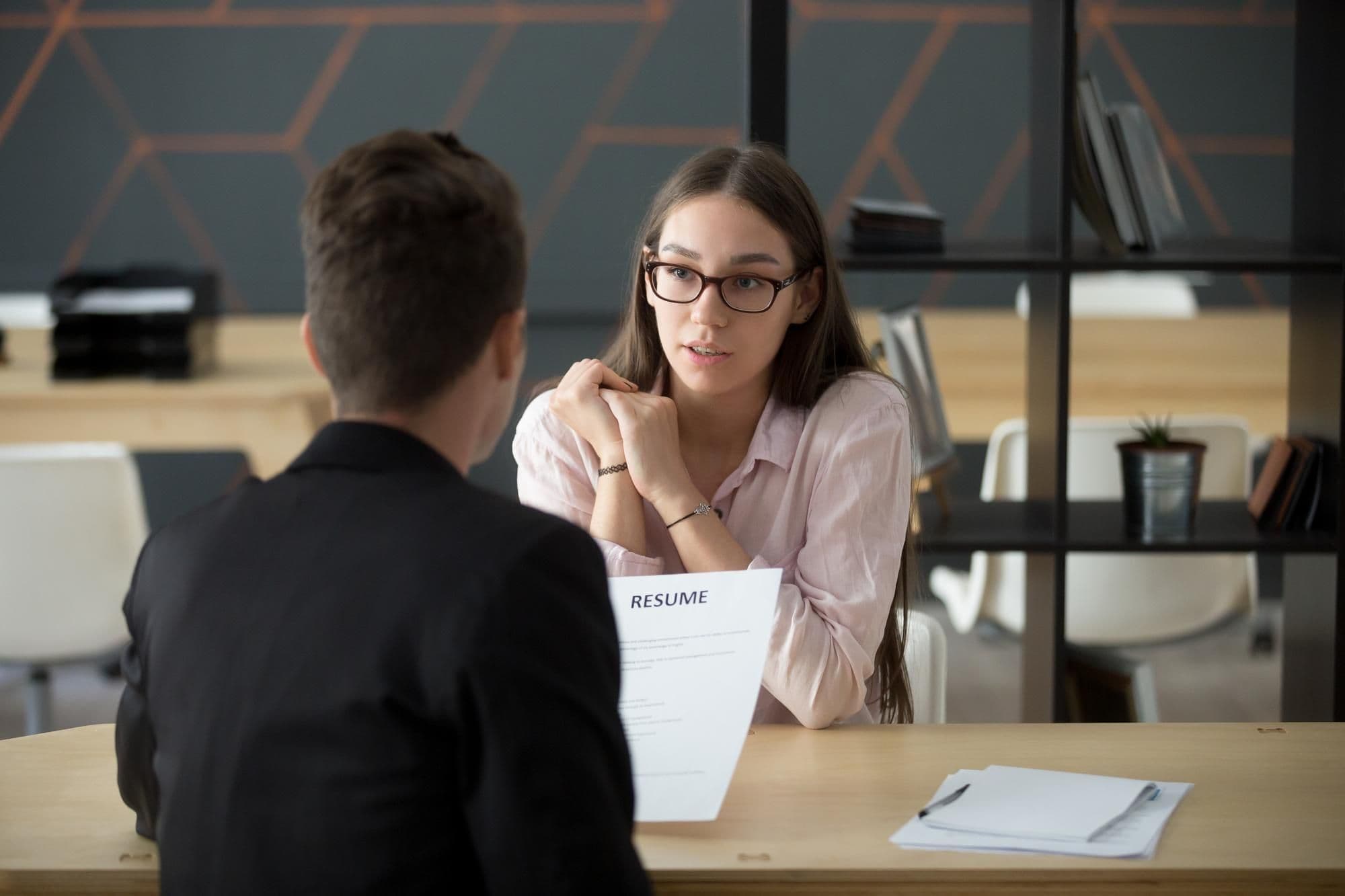 Confident millennial female applicant talking at job interview answering questions young serious candidate speaking to hr telling about work experience introduction and first impression concept