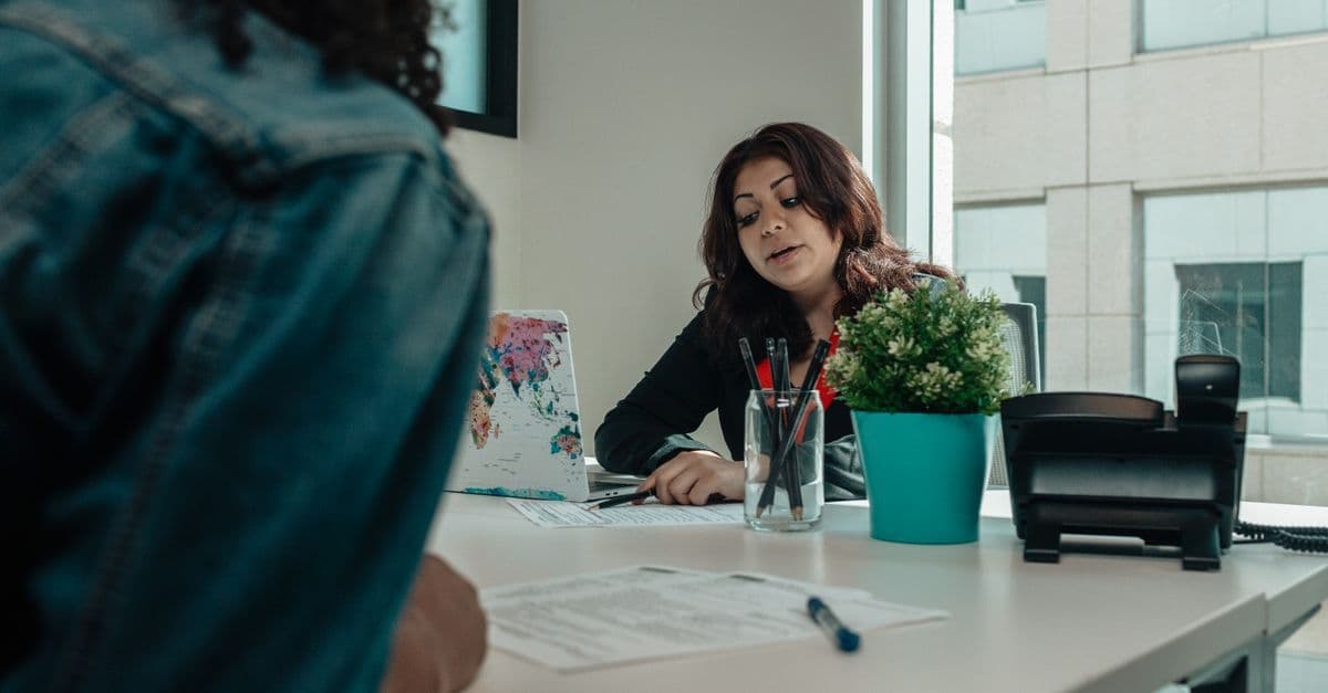 Two individuals in an office engaged in a discussion with paperwork.