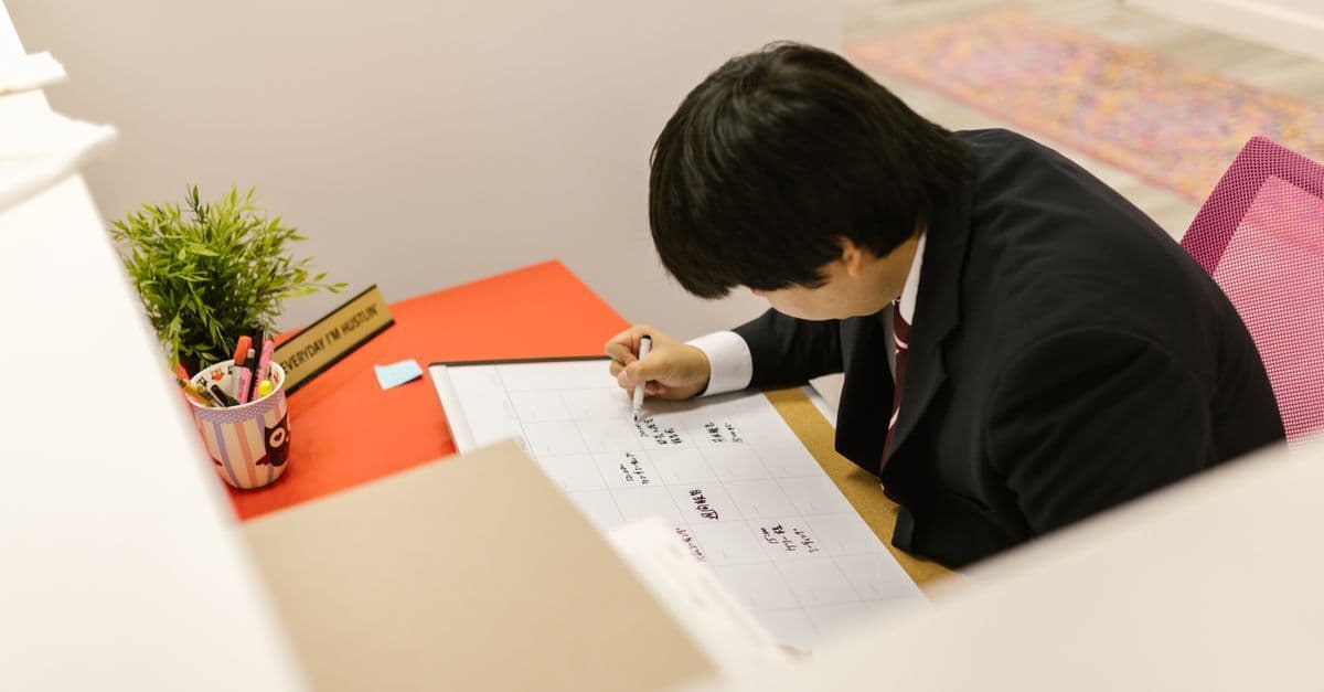 Business professional writing on monthly calendar at desk in modern office.