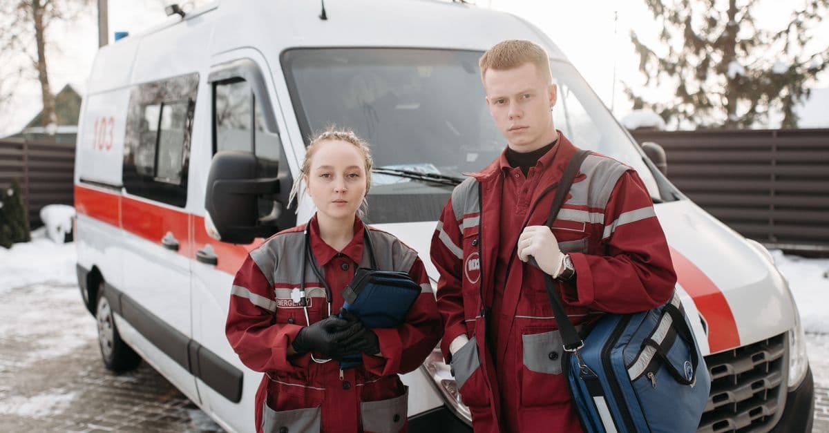 Two paramedics in uniforms standing by an ambulance in a winter setting, ready for emergency response.