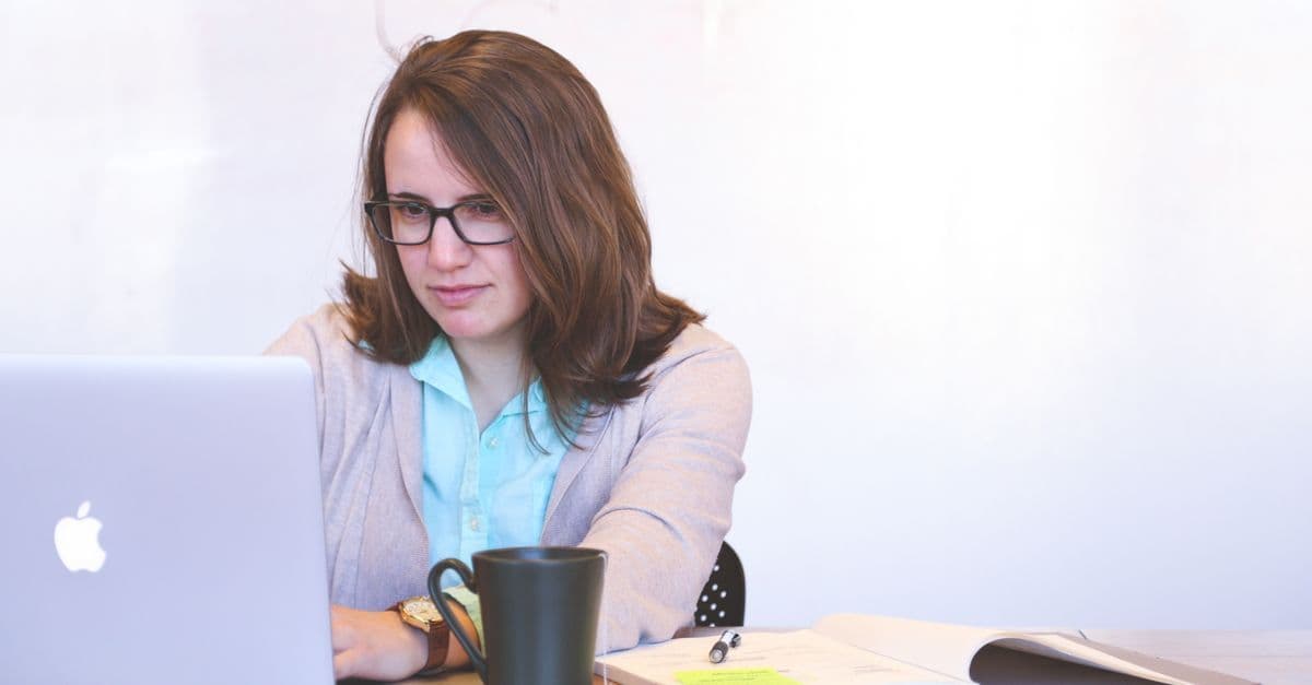 Focused businesswoman using a laptop at a desk with a mug and open notebook.