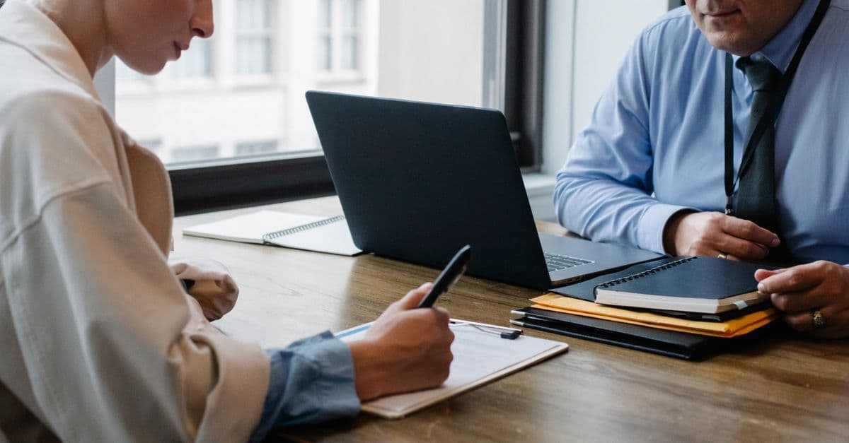 Crop faceless colleagues in formal clothes sitting at table with laptop and folder and signing documents while working together