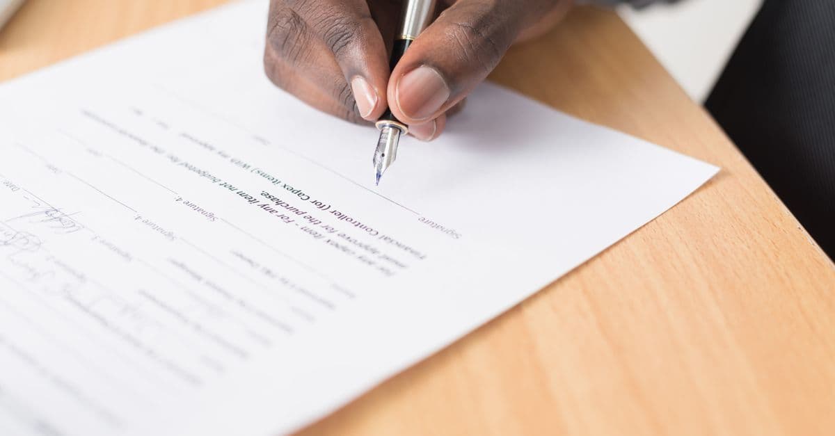 Person unterschreibt ein Antragsschreiben für die Elternzeit am Schreibtisch