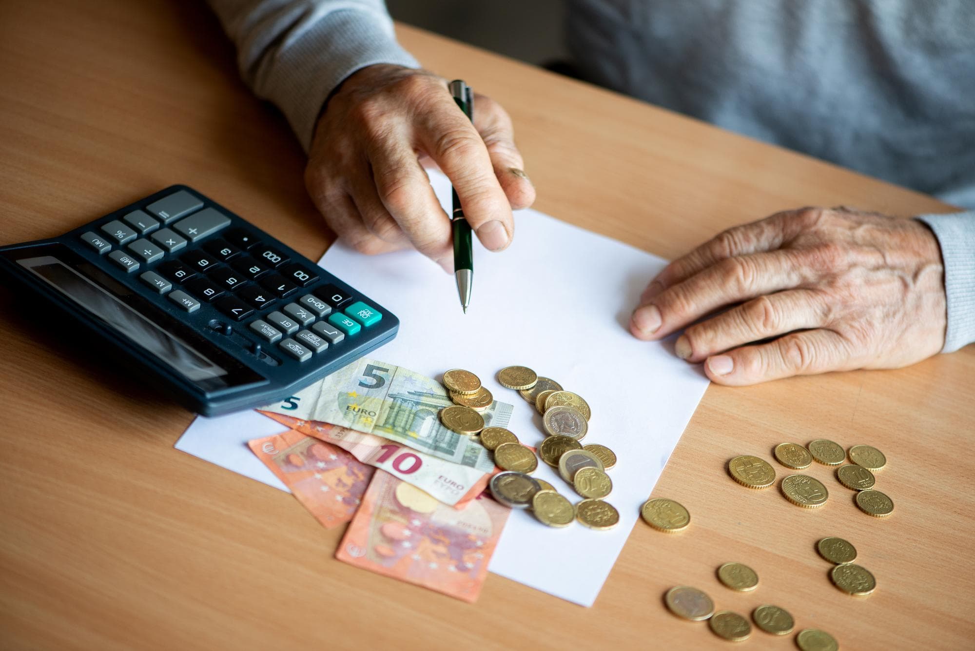 Rentner berechnet mit Taschenrechner und Euro-Münzen, was von der Durchschnittsrente netto übrig bleibt