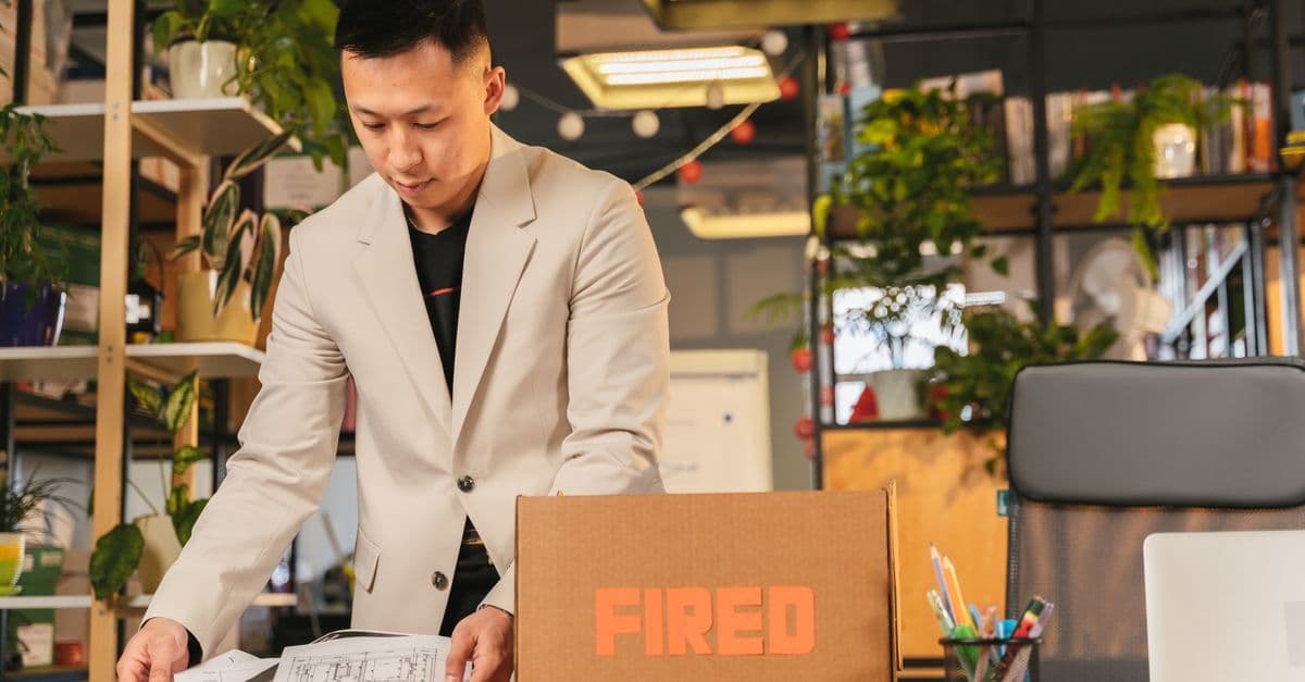 An employee packing documents into a box labeled 'FIRED' in an office environment.