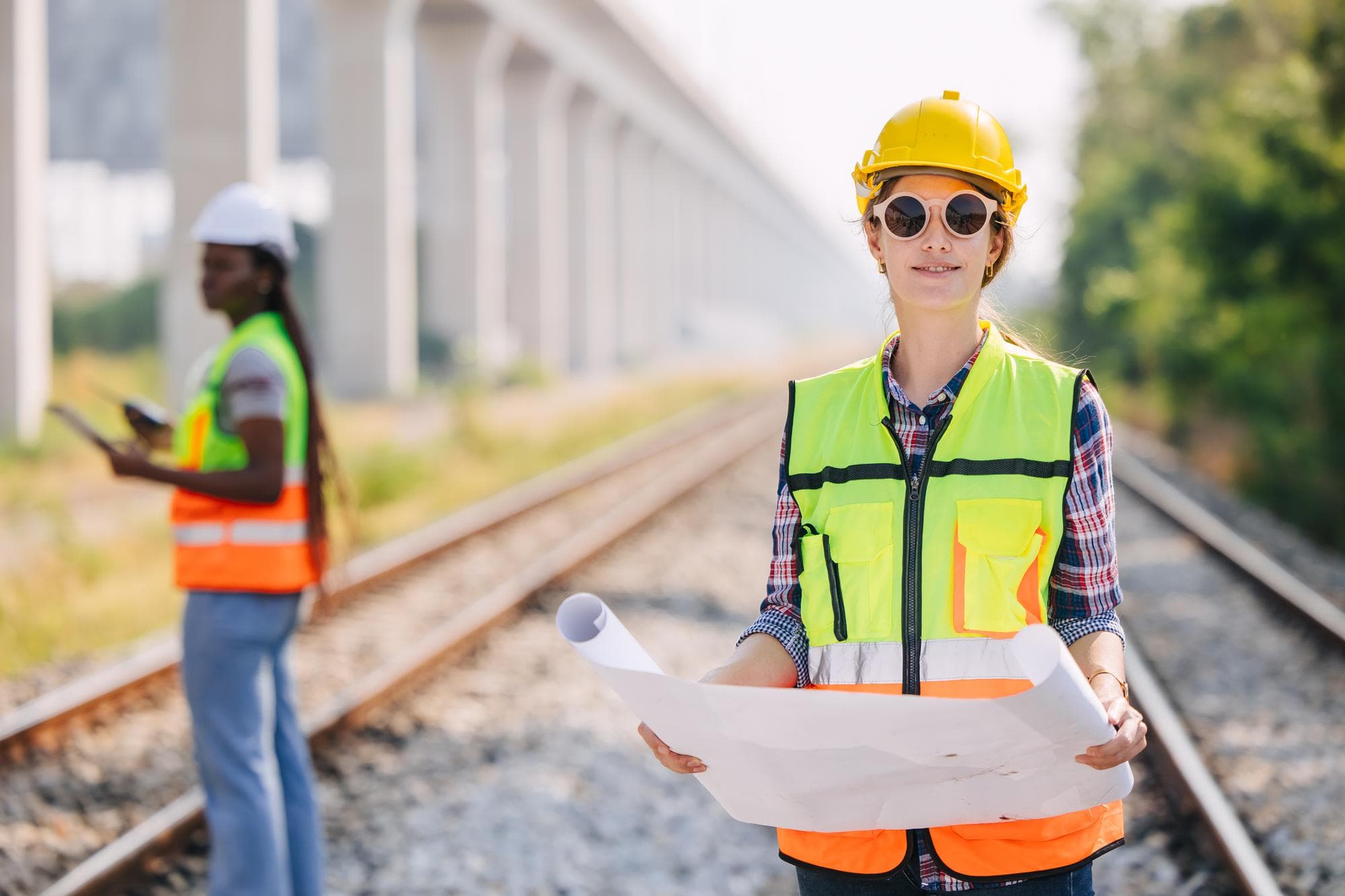 Ingenieurin mit gerolltem Bauplan an einer Bahnbaustelle – sinnbildlich für die Ingenieurwesen-Studiengänge der Deutschen Bahn