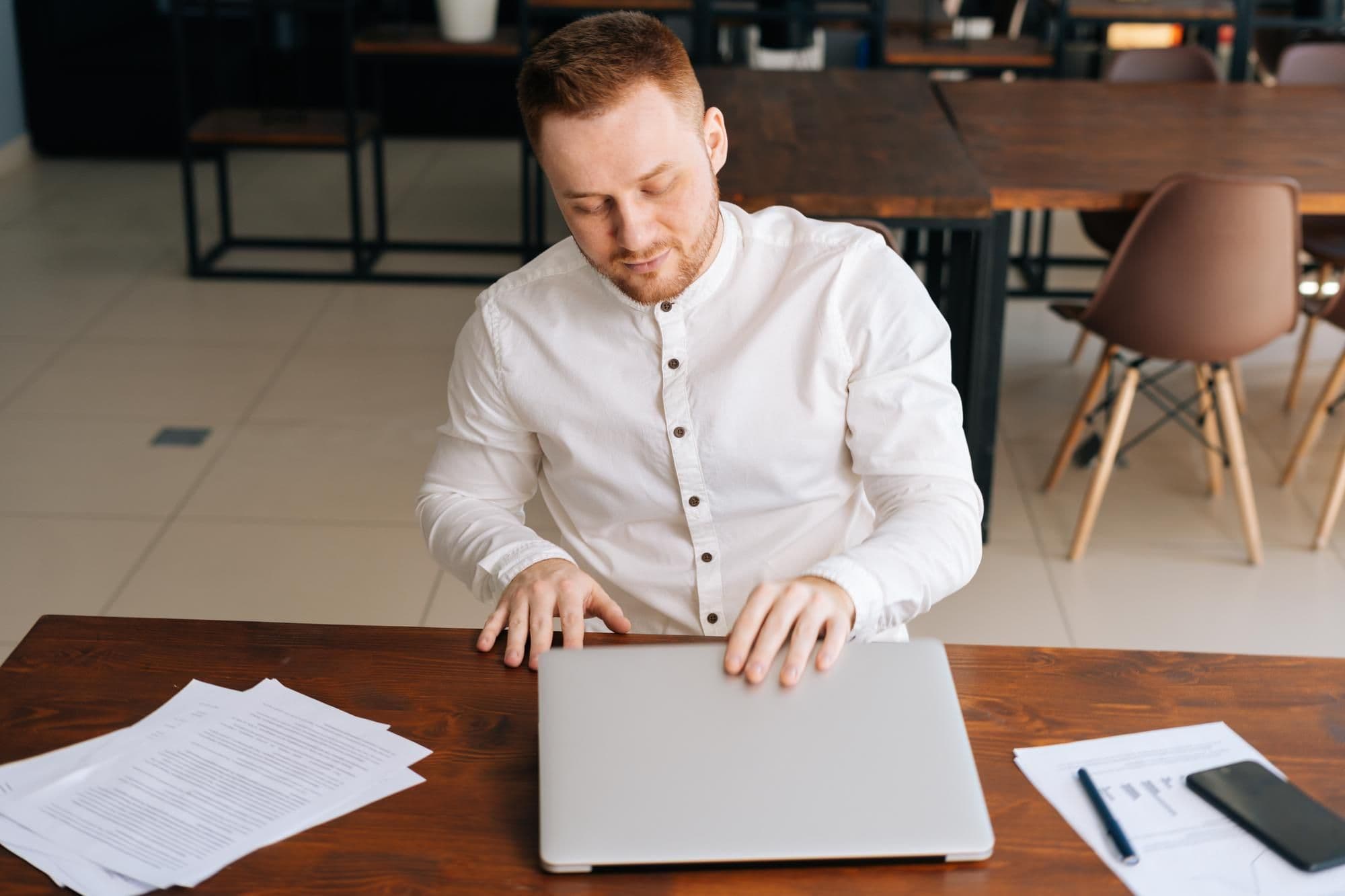 UFA RUSSIA 3 MAY 2020 Professional young businessman wearing fashion casual clothing is closing on laptop lid at the table in modern office room Concept of office working