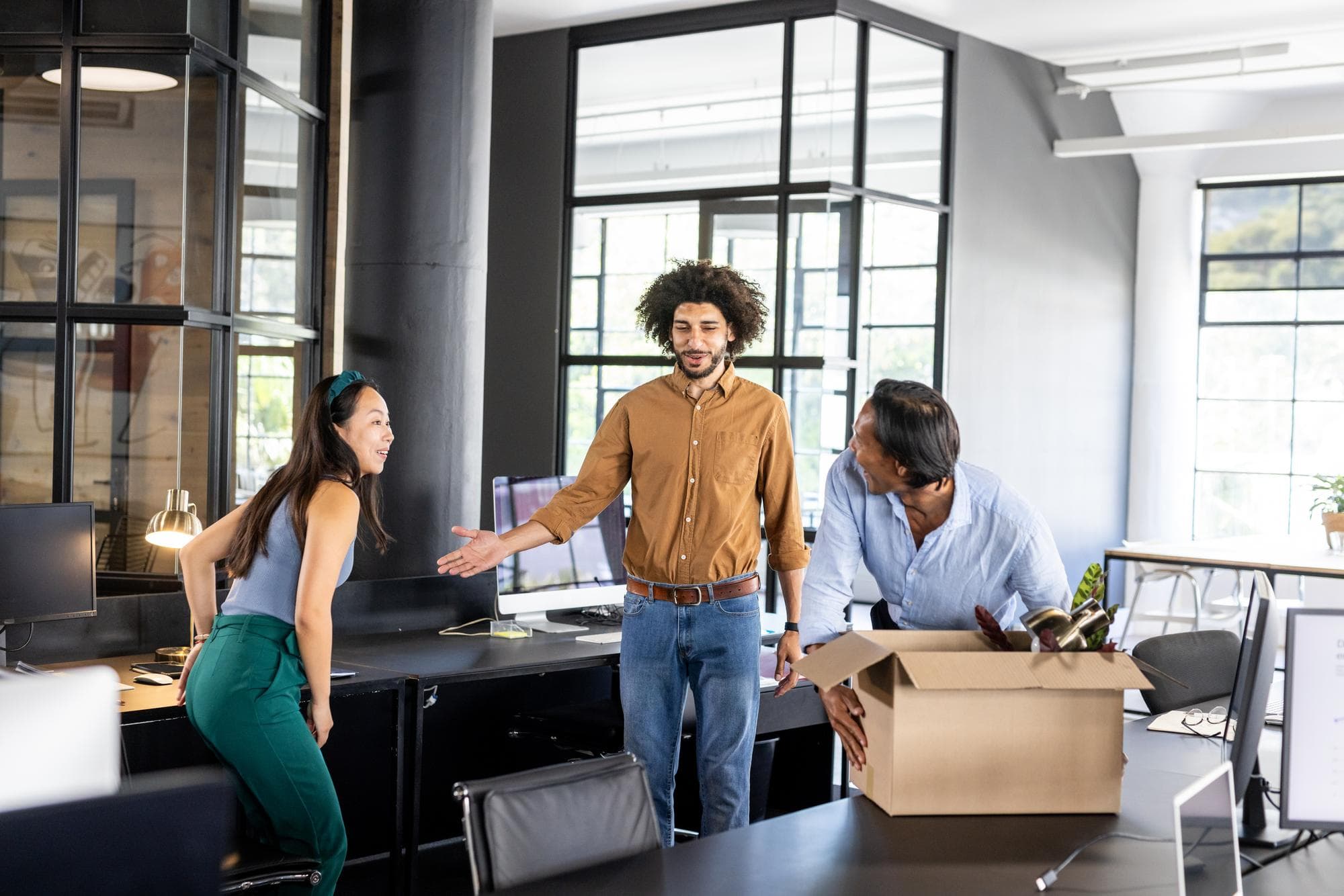 Colleagues welcoming new team member with box of belongings in modern office