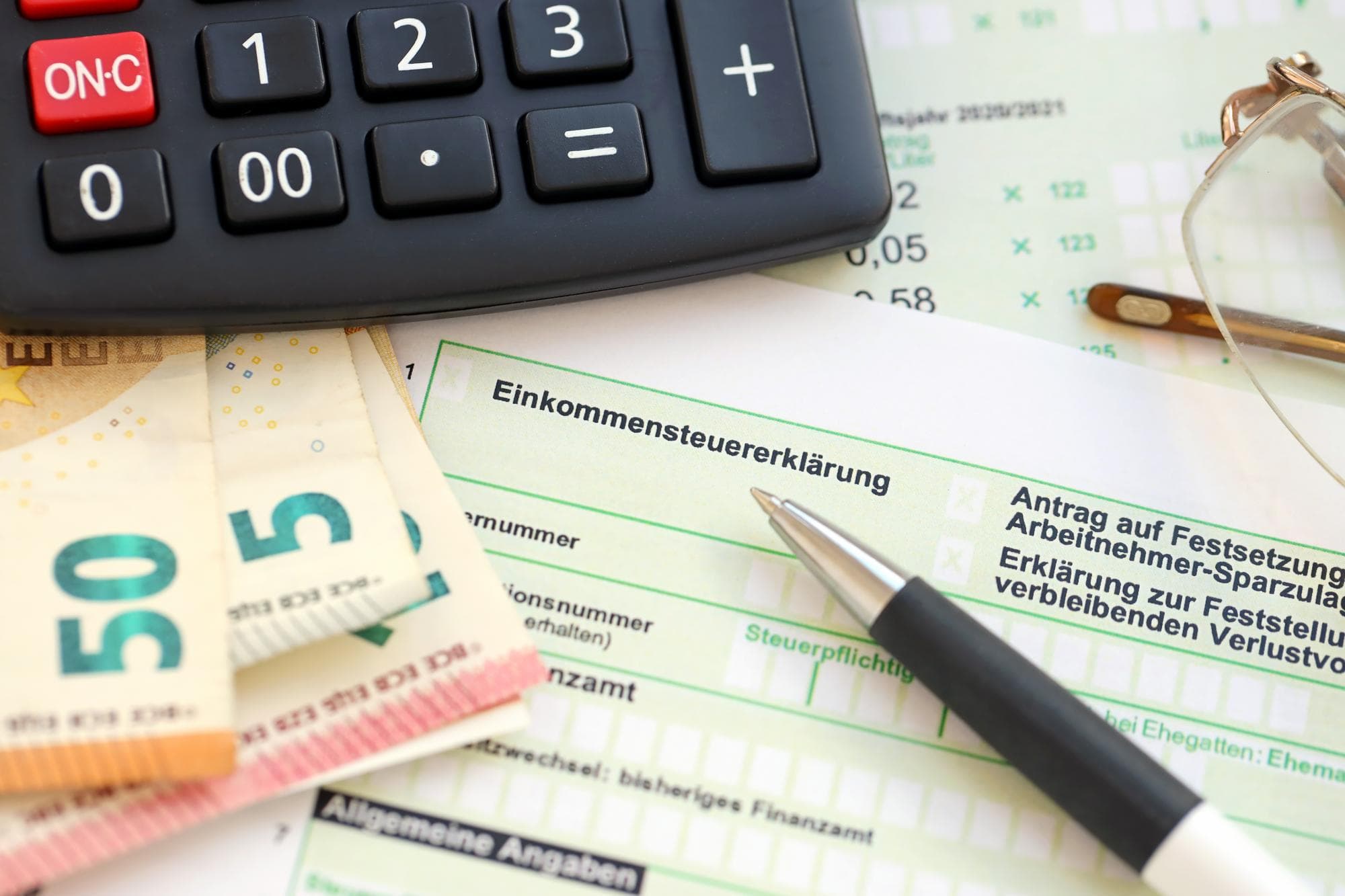 Taschenrechner, Steuerformulare und Geldscheine symbolisieren die Steuererklärung und mögliche Rückerstattung für Werkstudenten