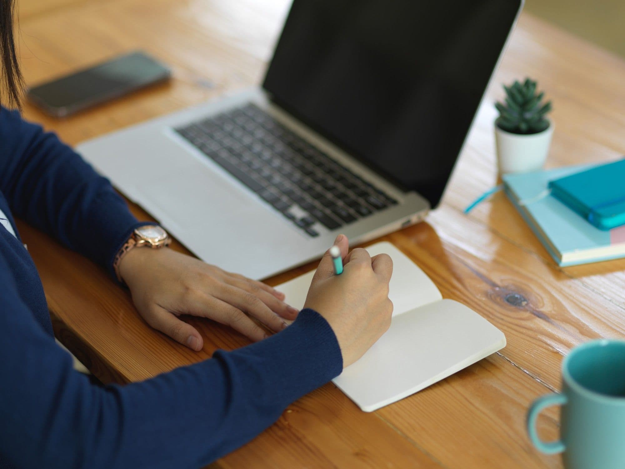 Studentin schreibt ein Anschreiben für die Praktikumsbewerbung am Schreibtisch mit Laptop und Notizen