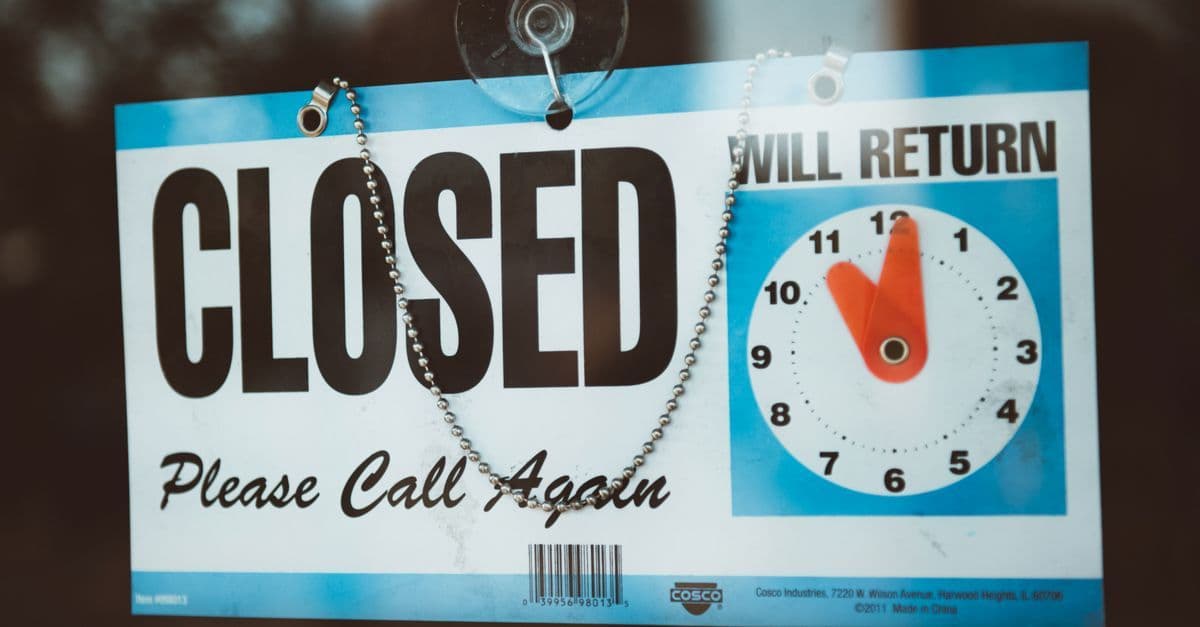 A close-up view of a 'Closed' sign on a door, displaying a return time.