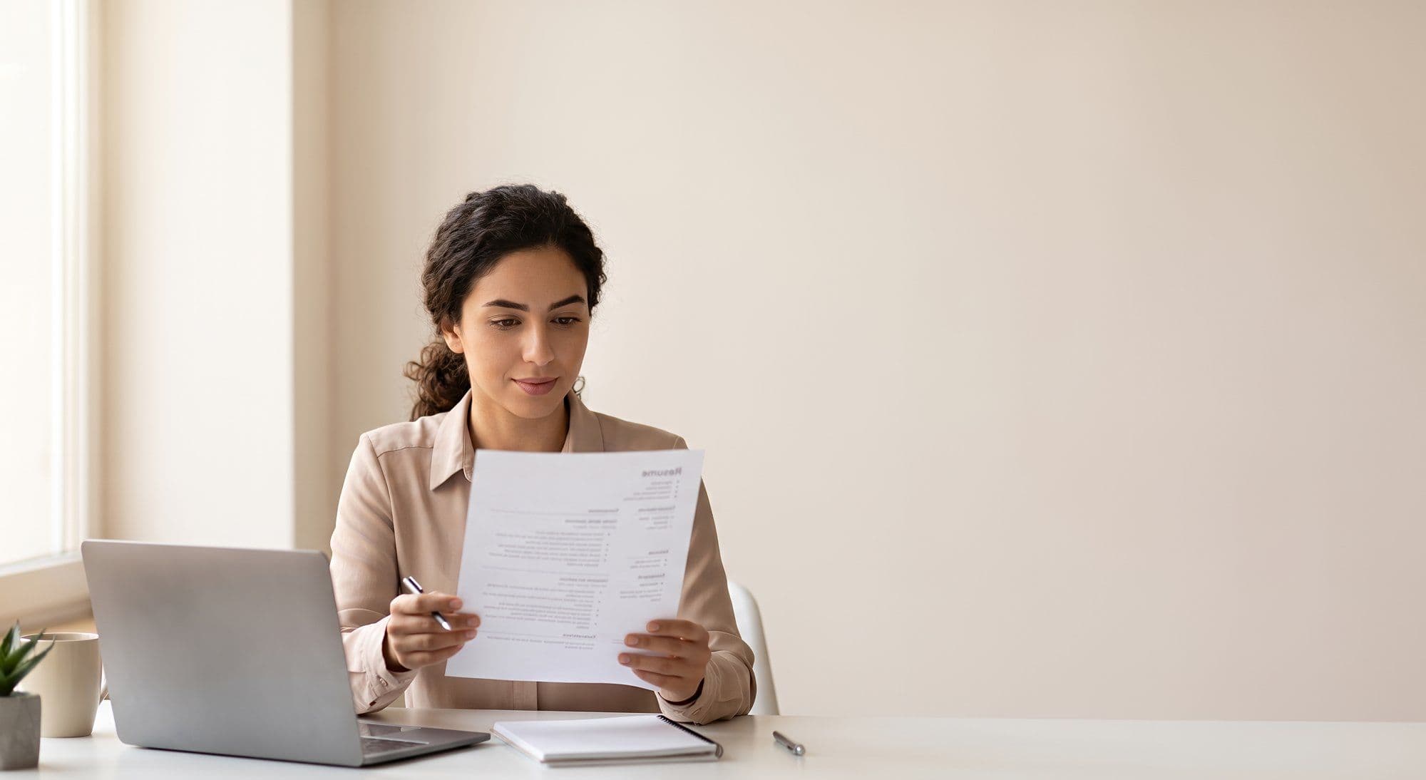 Young woman reviewing resume at desk with laptop and copy space