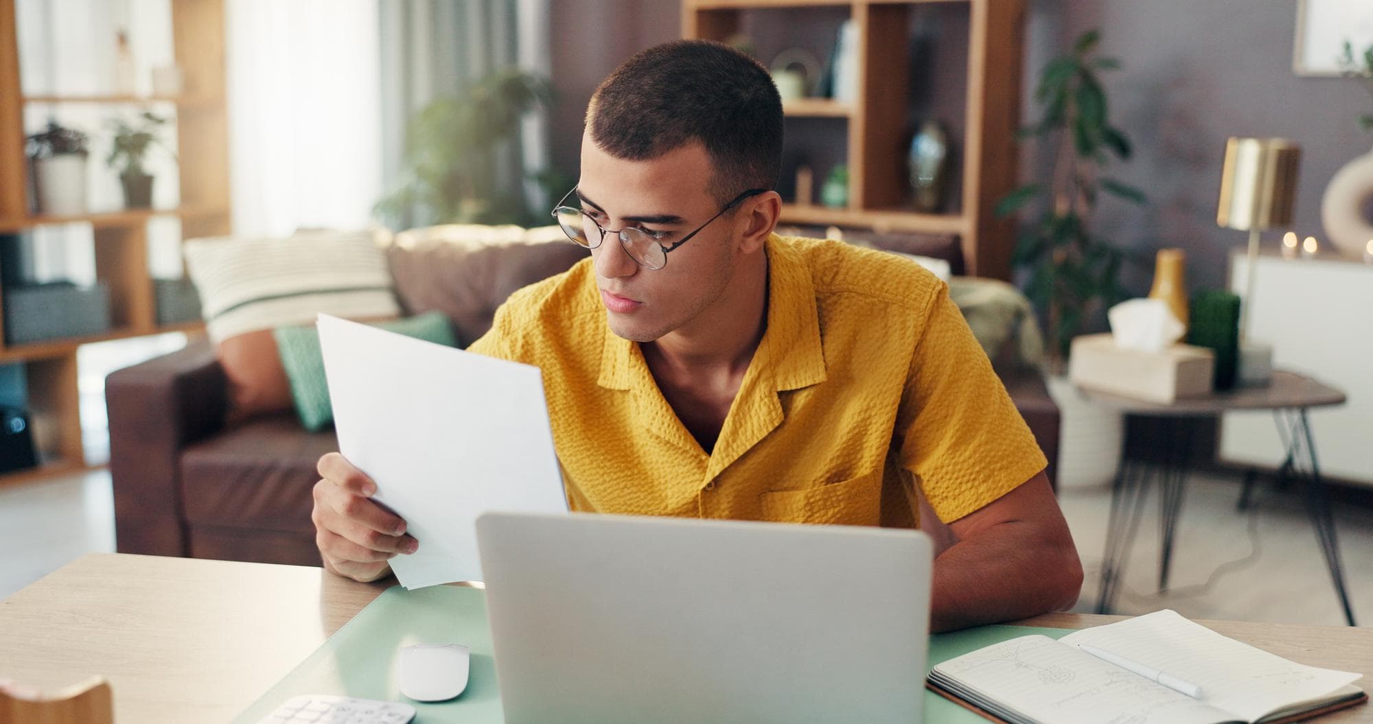 Man documents and finance with laptop for budget planning expenses or invoices at home Male person freelancer or remote work with paperwork on computer for financial report or audit at house