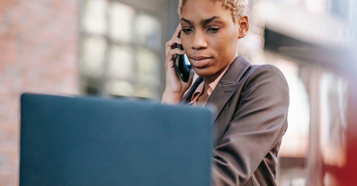 Low angle serious African American female entrepreneur having phone call and browsing netbook during outdoor work