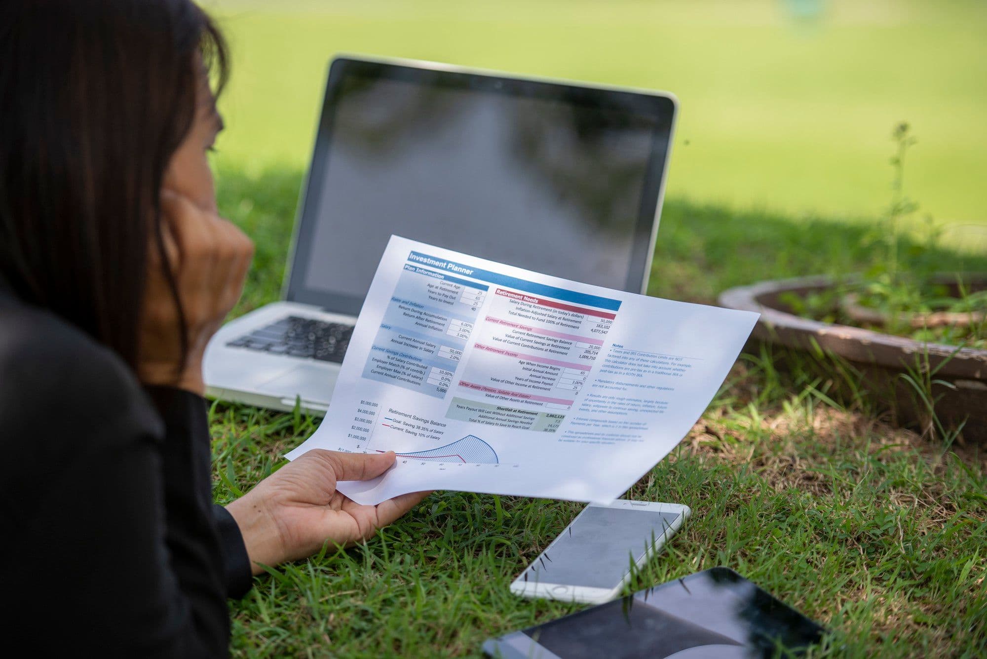 Frau arbeitet mit Laptop im Freien an Finanzunterlagen mit Diagrammen und Grafiken