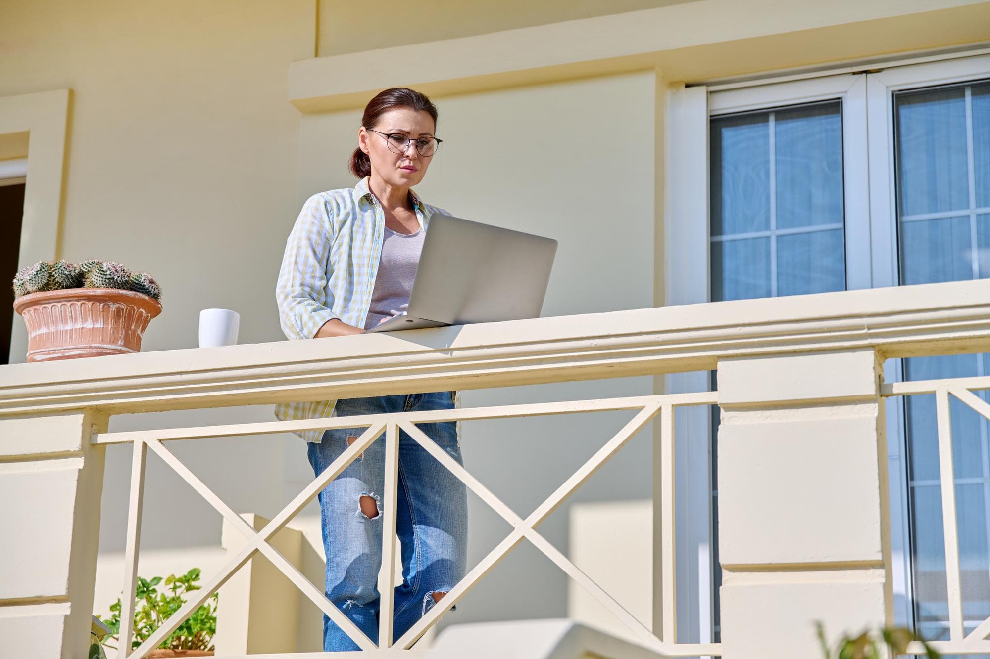 Middle aged woman with laptop on the porch of the house